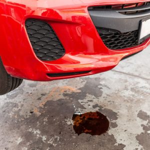 A red car with fluid leaking on the pavement.