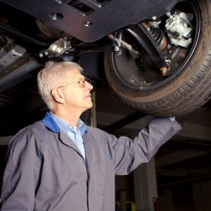 mechanic standing under a car looking at the car wheel