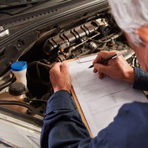 someone filling out a checklist standing in front of a car engine 